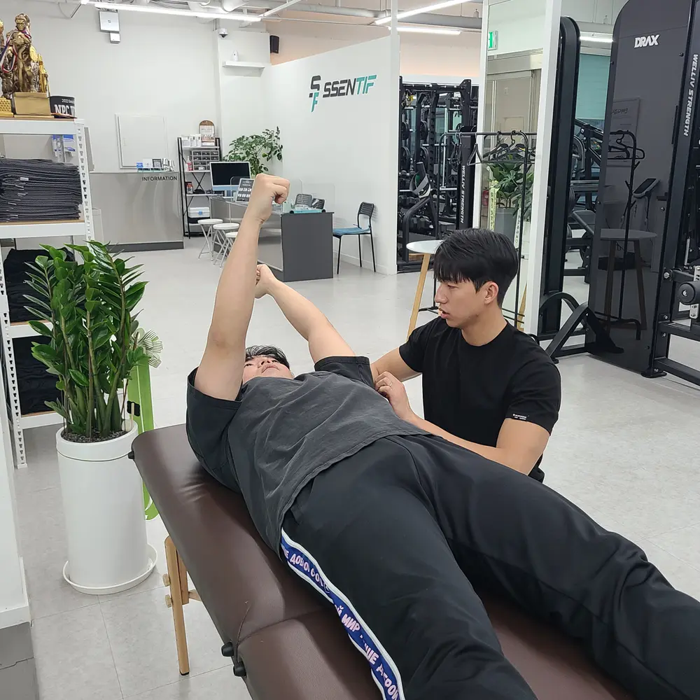 코치가 베드에 누운 회원의 어깨와 팔 가동범위를 잡아주는 모습